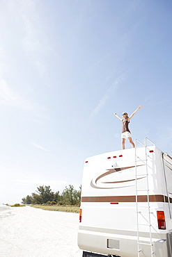 Woman standing on motor home with arms outstretched