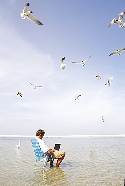 Man sitting in ocean surf with laptop