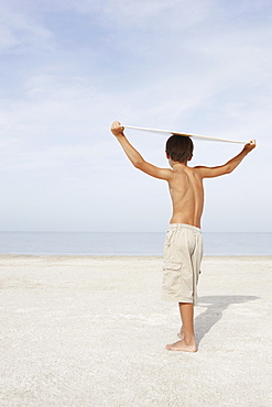 Boy standing on beach holding bodyboard overhead