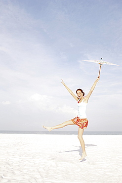 Girl holding umbrella and dancing on beach