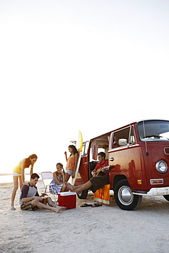 Friends socializing around van on beach