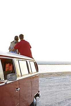 Couple watching ocean sunset from top of van