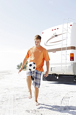 Young man playing with soccer ball on beach