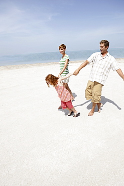 Girl holding hands with mother and father on beach