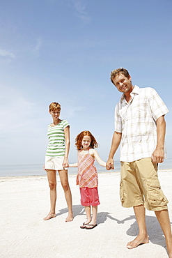 Girl holding hands with mother and father on beach