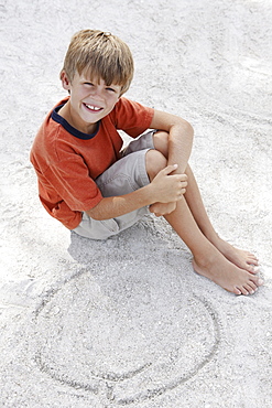 Boy drawing designs in beach sand