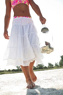 Girl on beach carrying jar of shells