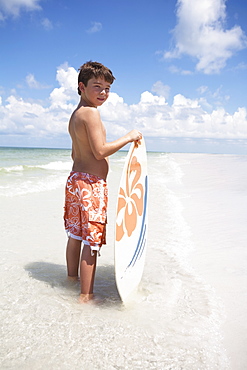 Boy holding skimboard in ocean