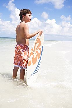 Boy holding skimboard in ocean