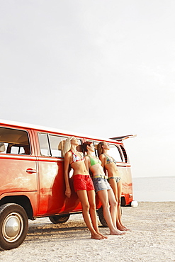 Young women leaning against van on beach