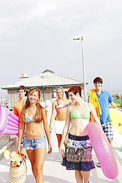 Friends carrying beach essentials on boardwalk 