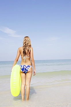 Teenage girl holding inflatable ring contemplating ocean waves