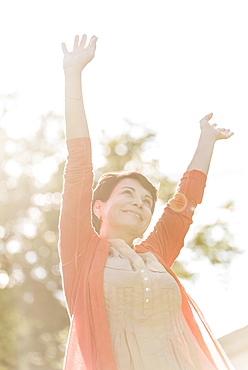 Mature woman raising hands in sunlight