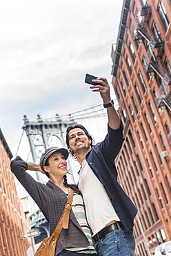 Couple taking selfie on street, Brooklyn Bridge in background, Brooklyn, New York