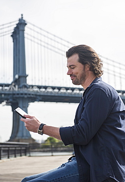 Man using tablet pc, Manhattan Bridge in background, Brooklyn, New York