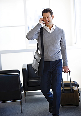 Businessman pulling suitcase and talking on mobile phone in airport lounge