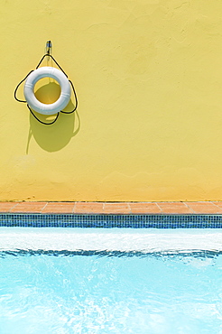 Lifebelt hanging on yellow wall by swimming pool