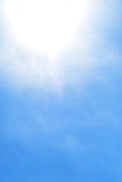 Sun behind small cloud on blue sky