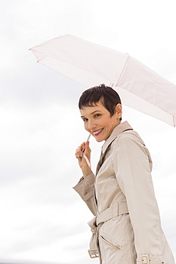 Portrait of smiling woman wearing raincoat and holding umbrella
