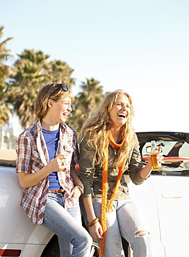 Two women drinking beer next to convertible