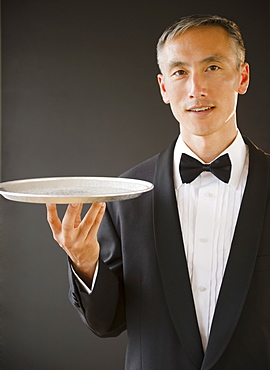 Waiter wearing bow tie and holding tray, studio shot