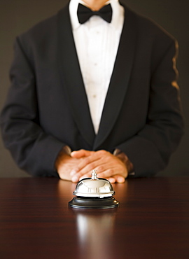 Service bell in the foreground, man wearing bow tie in the background, studio shot