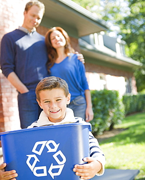 USA, New York, Flanders, Boy (8-9) holding bucket with recycling symbol, parents in background