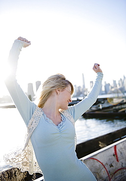 USA, Brooklyn, Williamsburg, Portrait of blonde woman stretching arms in backlit