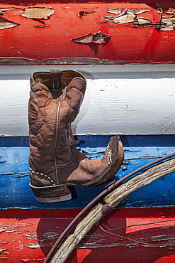 Cowboy boot and wagon wheel against red, white and blue peeling paint