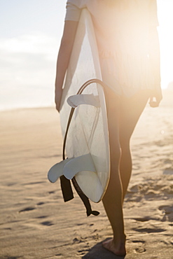 Female surfer walking on beach at sunset, Rockaway Beach, New York