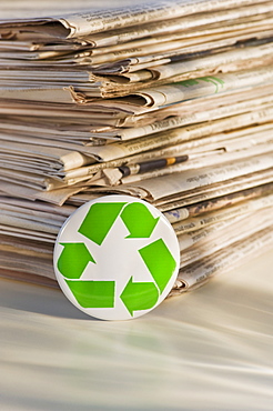 Recycling sign by pile of newspapers, studio shot