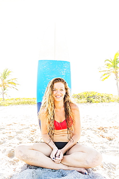 Portrait of young woman sitting on beach with surfboard in background, Jupiter, Florida