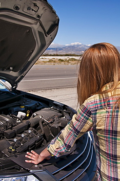 USA, California, Palm Springs, Woman standing in front of broken car in desert