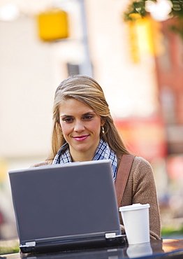 Young woman sitting with laptop in sidewalk cafe