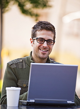 Young woman sitting with laptop in sidewalk cafe