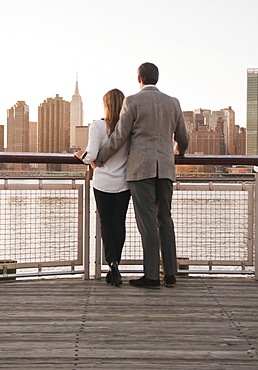 USA, New York, Long Island City, Rear view of young couple standing on boardwalk, Manhattan skyline in background