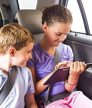 Boy (6-7) and girl (8-9) using digital tablet while sitting in car