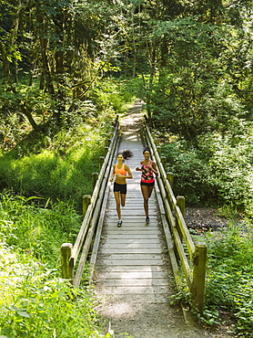 Two young women running over wooden footbridge, USA, Oregon, Portland