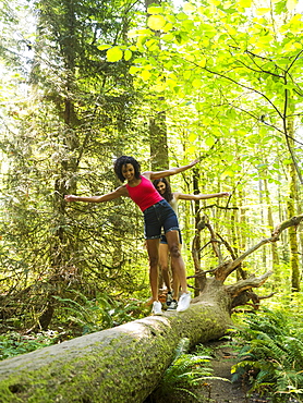 Two young women walking on log in forest, USA, Oregon, Portland