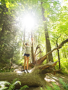 Young woman standing on log with arms raised, USA, Oregon, Portland