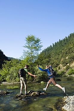 Hikers jumping across river on rocks