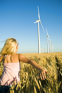 Girl running through tall wheat field on wind farm