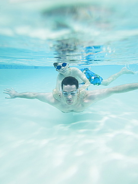 Boy swimming on fatherâ€™s back underwater