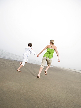 Mother and daughter holding hands and running on beach