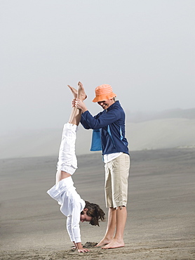 Mother holding daughter upside down on beach