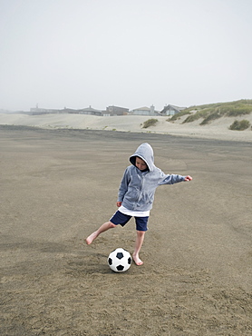 Boy kicking soccer ball on beach