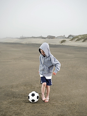 Boy kicking soccer ball on beach