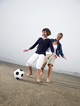 Mother and daughter kicking soccer ball on beach