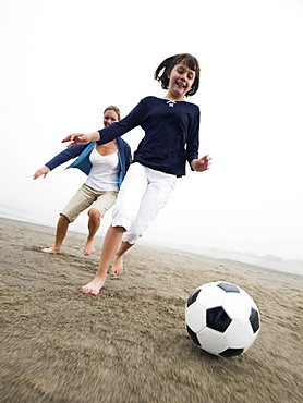 Mother and daughter playing soccer on beach