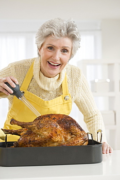 Senior woman basting roast turkey